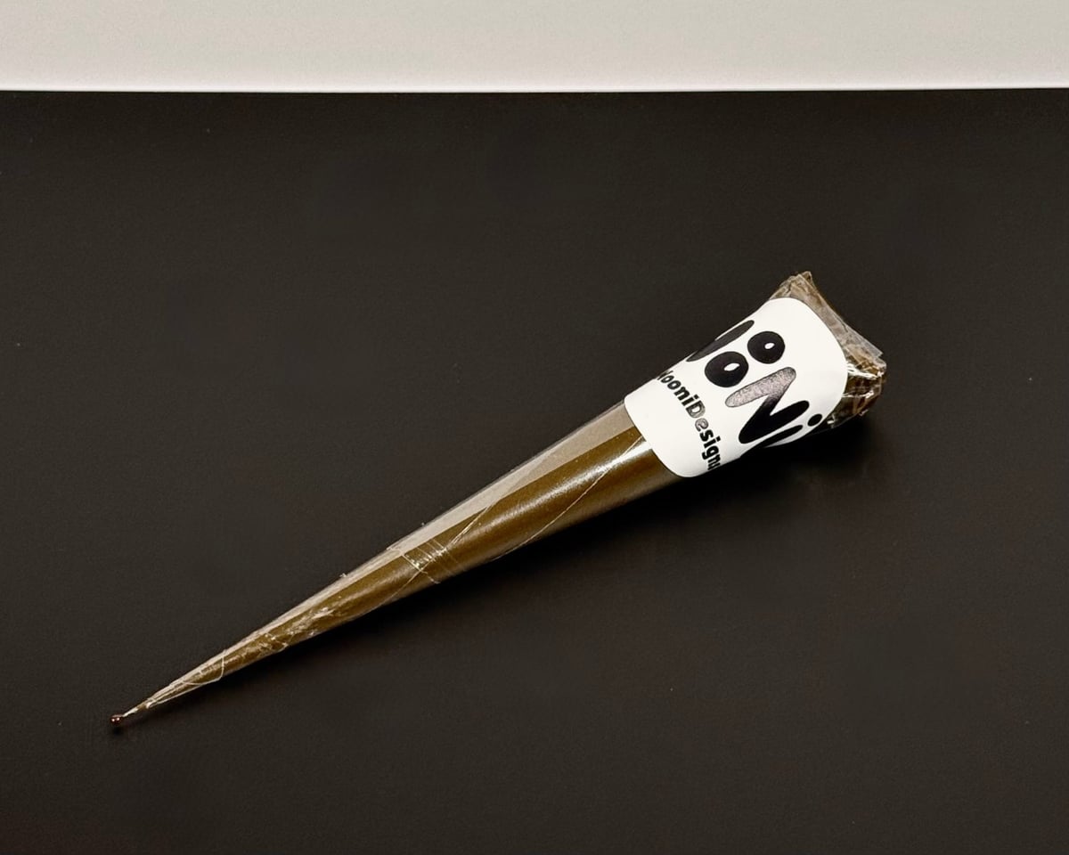 A single hand-rolled NooniDesigns henna cone with a fine tapered tip and a white NooniDesigns sticker around the base.